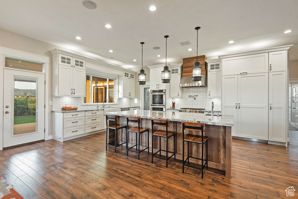 Kitchen with appliances with stainless steel finishes, dark wood finished floors, white cabinetry, a kitchen breakfast bar, and backsplash