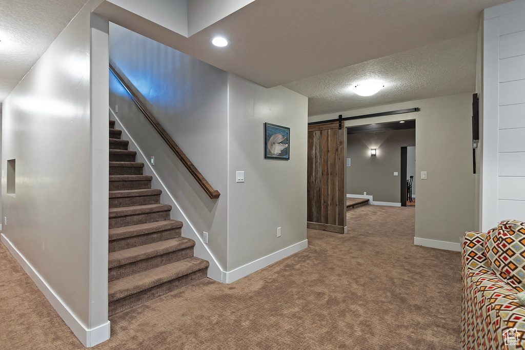 Stairs with a barn door, carpet floors, a textured ceiling, baseboards, and recessed lighting