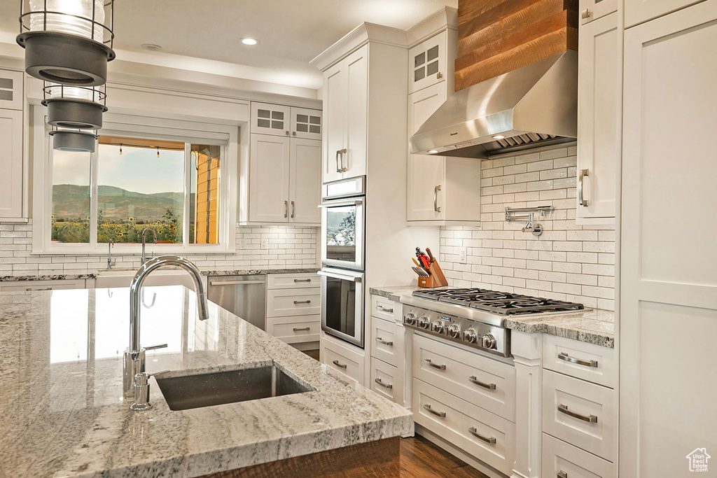Kitchen featuring wall chimney range hood, stainless steel appliances, a sink, white cabinetry, and recessed lighting