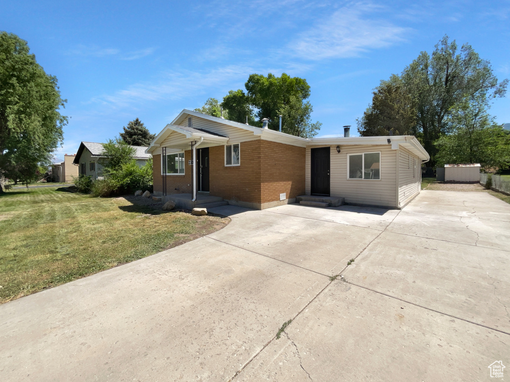Ranch-style home featuring brick siding, a front lawn, concrete driveway, and a storage unit