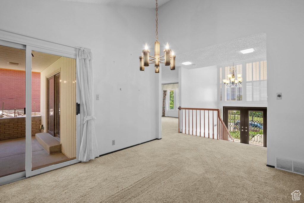Carpeted empty room featuring a chandelier and a towering ceiling