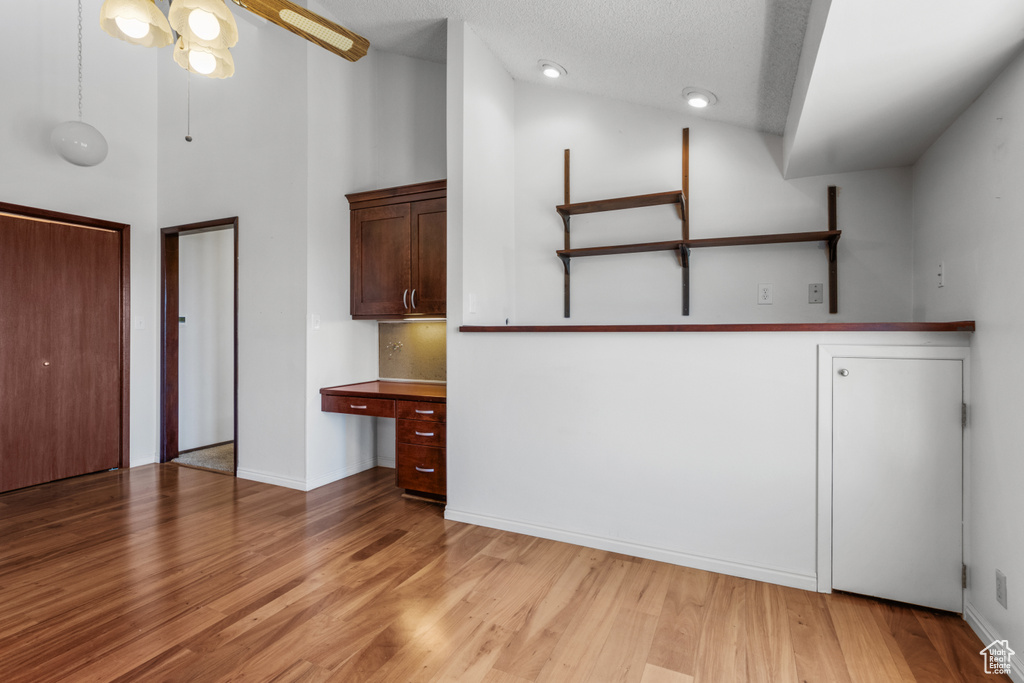 Interior space with light wood finished floors, built in desk, a towering ceiling, and ceiling fan