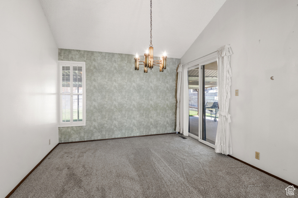 Carpeted empty room featuring vaulted ceiling and a chandelier