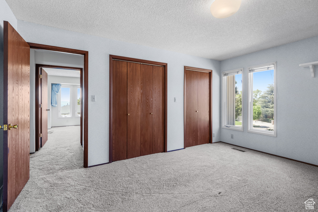 Unfurnished bedroom featuring carpet, two closets, and a textured ceiling