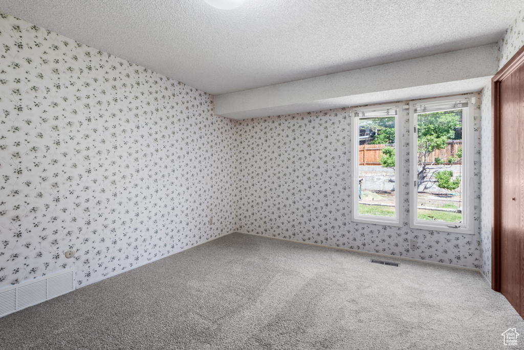 Carpeted spare room with wallpapered walls and a textured ceiling