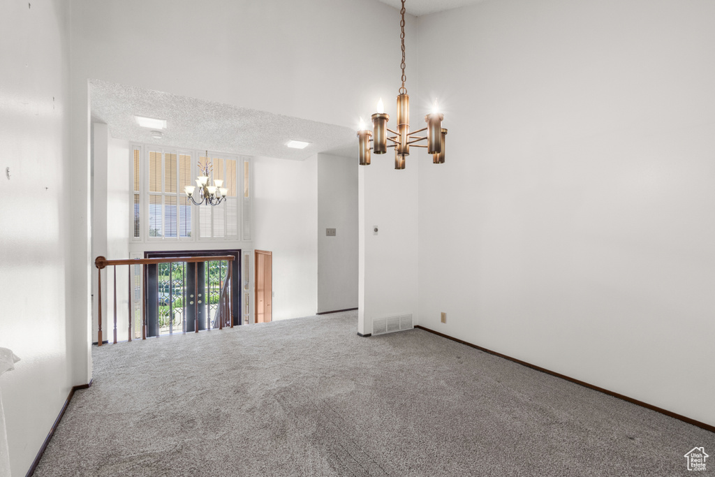 Empty room featuring a chandelier, carpet, and a high ceiling