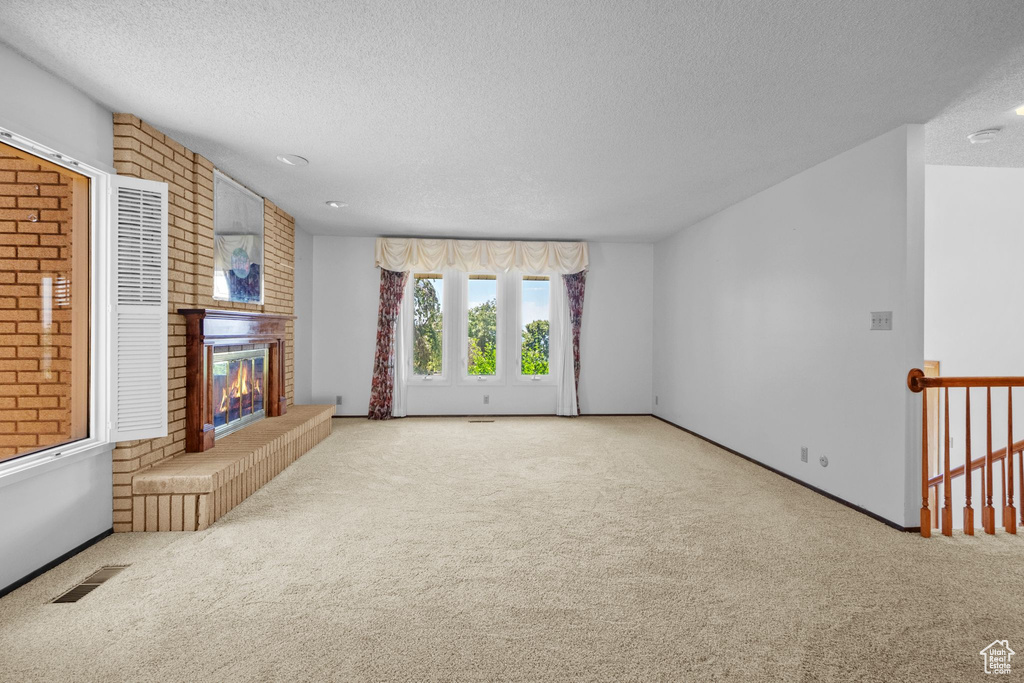 Unfurnished living room featuring a textured ceiling, carpet floors, and a fireplace