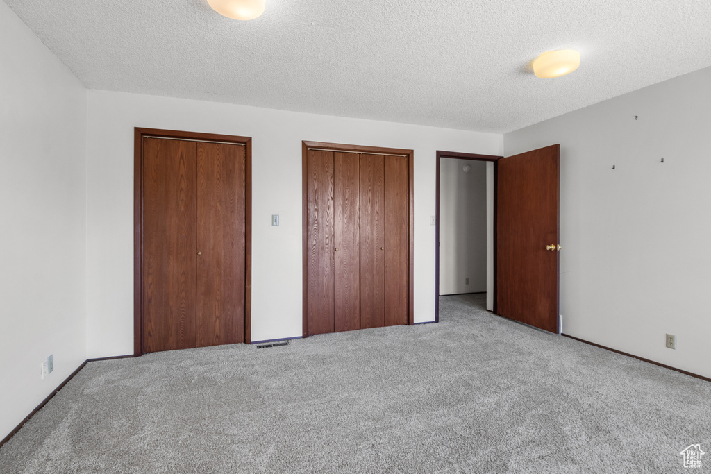 Unfurnished bedroom with two closets, carpet flooring, and a textured ceiling