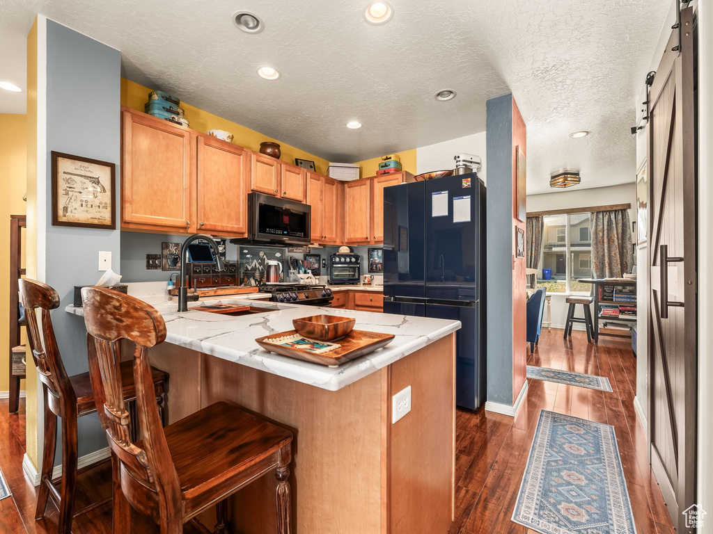 Kitchen with black appliances, a peninsula, dark wood-style floors, recessed lighting, and a breakfast bar area