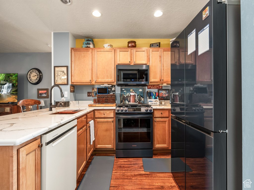 Kitchen featuring black appliances, a peninsula, dark wood-style floors, recessed lighting, and a textured ceiling