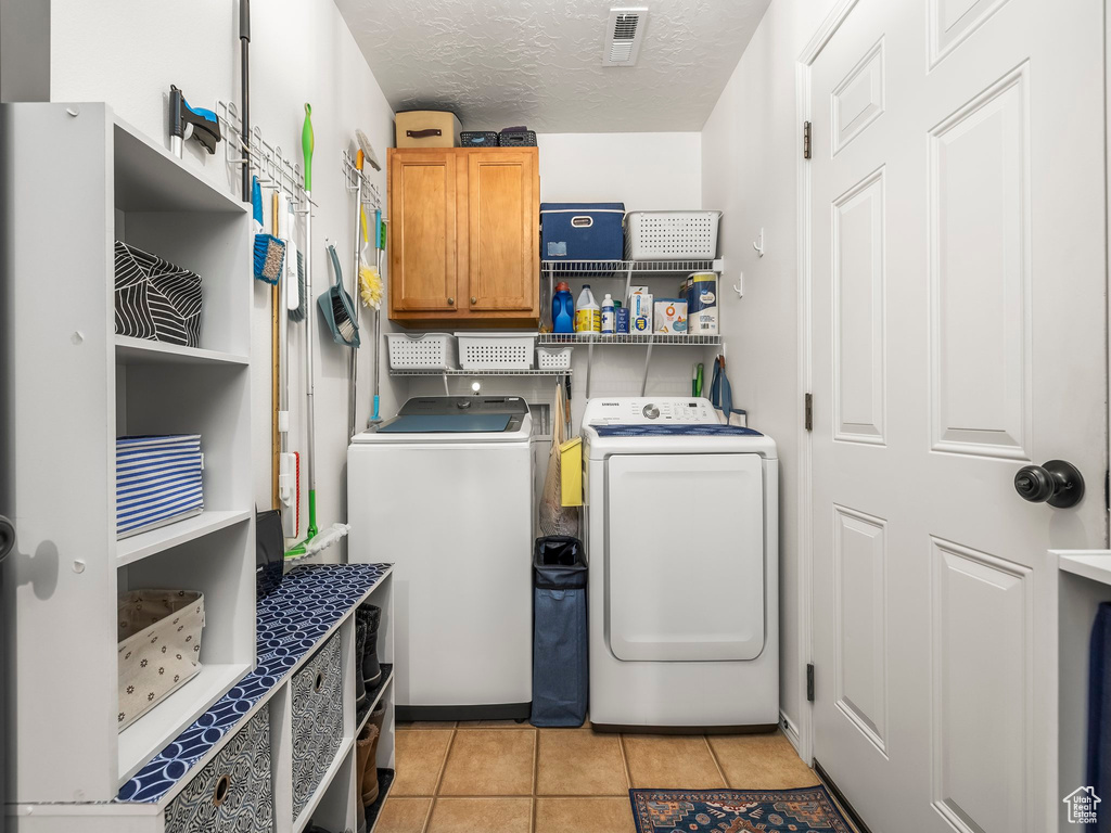 Laundry area featuring washing machine and clothes dryer, cabinet space, light tile patterned floors, and a textured ceiling