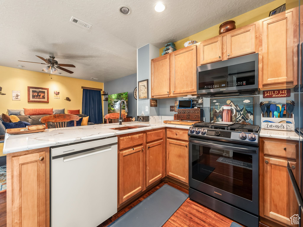 Kitchen with dishwasher, gas stove, a peninsula, open floor plan, and wood finished floors
