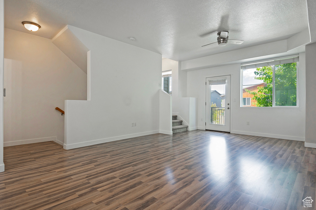 Unfurnished living room with plenty of natural light, dark wood-style floors, a textured ceiling, ceiling fan, and stairway