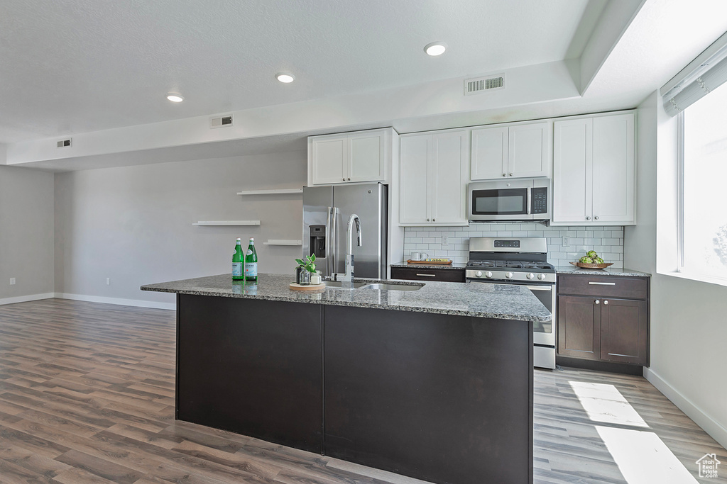 Kitchen featuring appliances with stainless steel finishes, wood finished floors, backsplash, dark stone counters, and recessed lighting