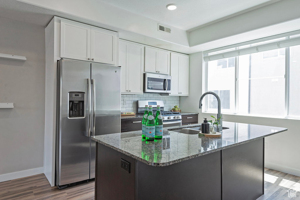 Kitchen with stainless steel appliances, wood finished floors, white cabinets, stone countertops, and decorative backsplash