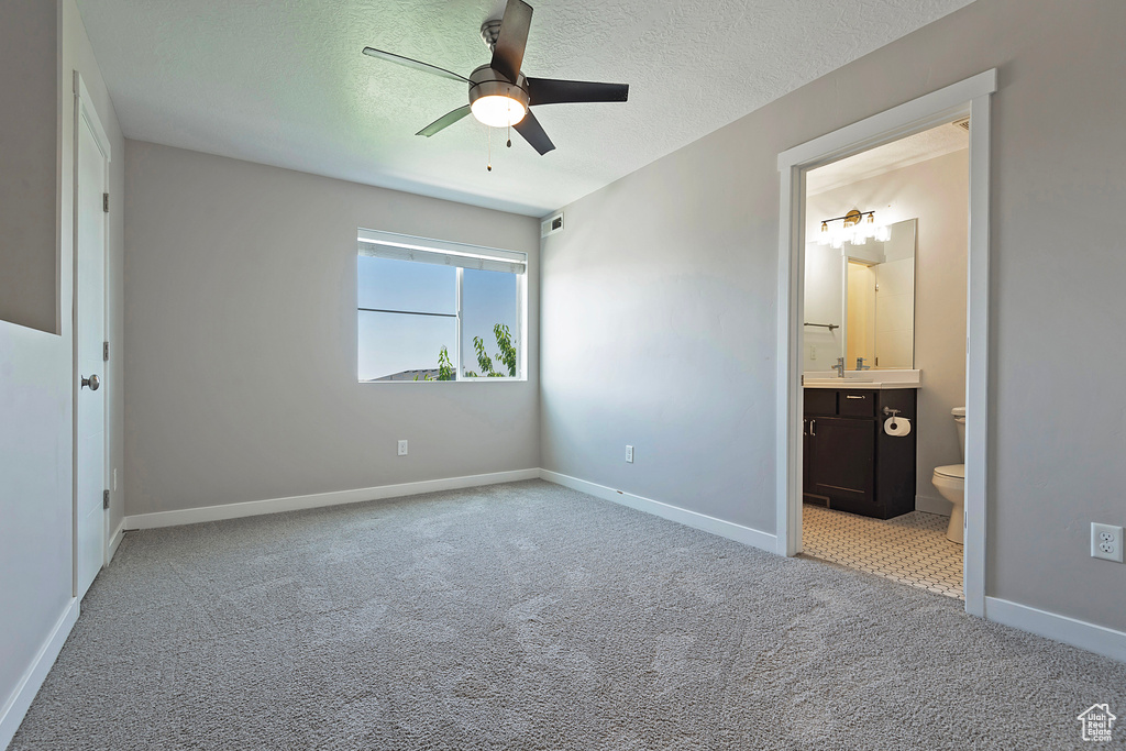 Unfurnished bedroom with light colored carpet, a textured ceiling, ensuite bath, and ceiling fan