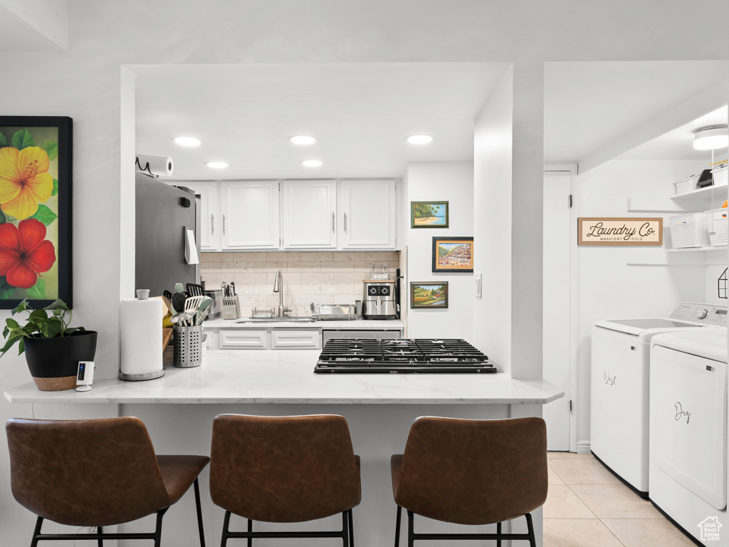 Kitchen featuring washing machine and clothes dryer, a peninsula, white cabinets, a breakfast bar, and tasteful backsplash