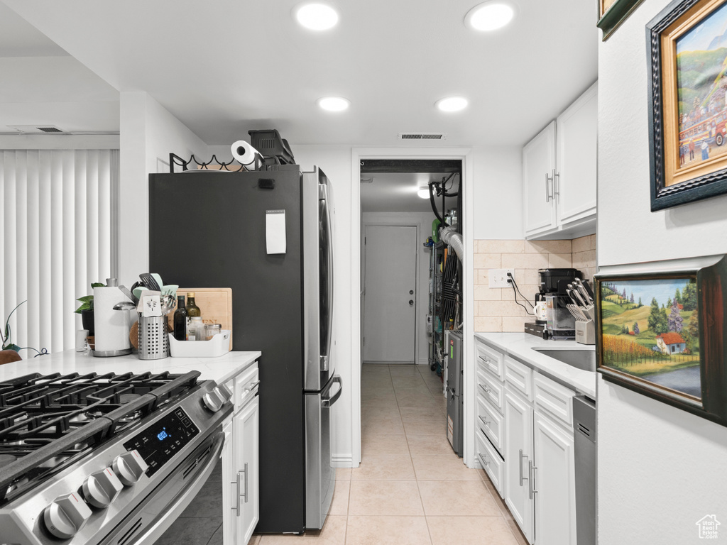 Kitchen with light tile patterned floors, white cabinets, stainless steel appliances, decorative backsplash, and recessed lighting