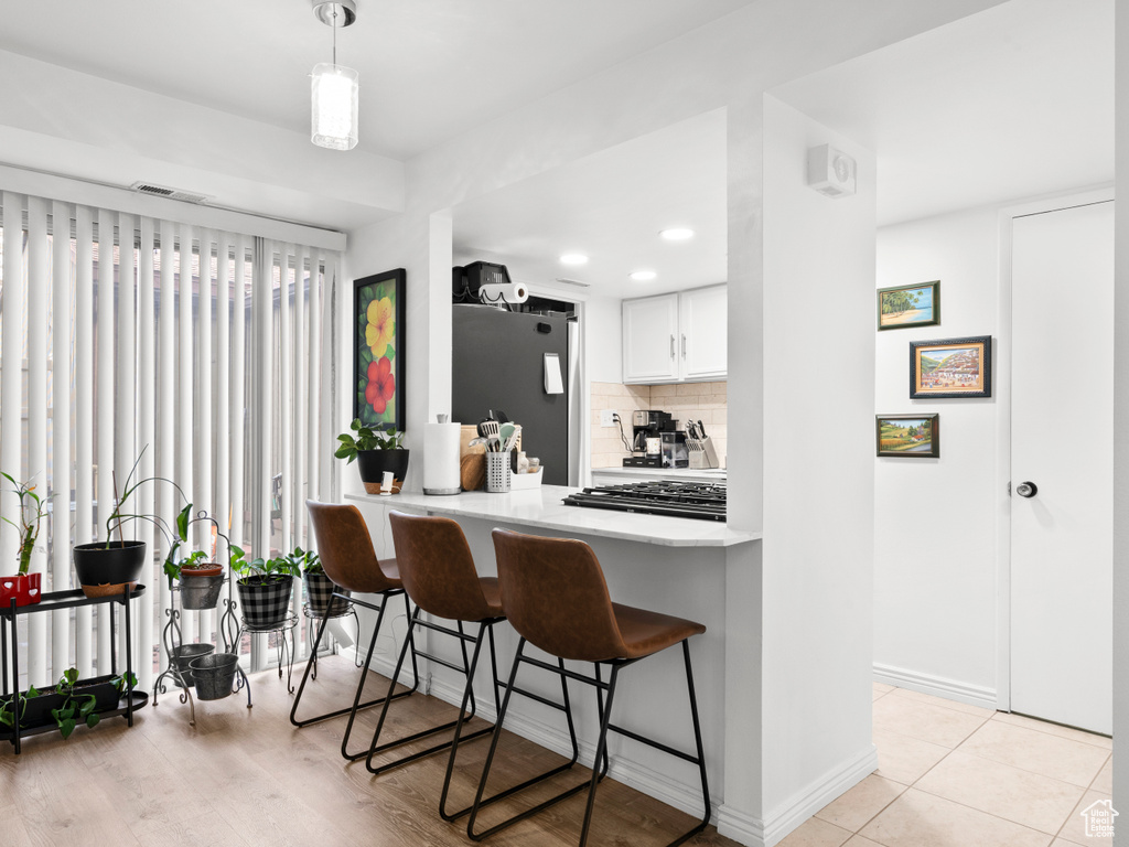 Kitchen featuring freestanding refrigerator, tasteful backsplash, a kitchen breakfast bar, light countertops, and white cabinetry
