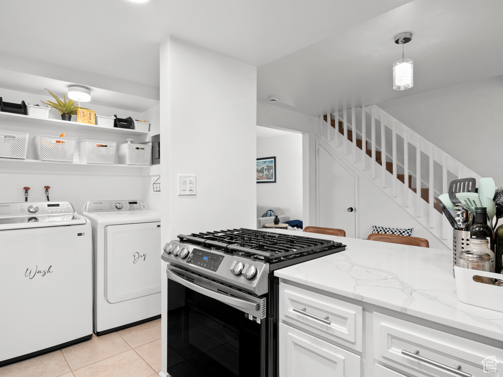 Kitchen with stainless steel gas stove, washer and clothes dryer, light tile patterned floors, white cabinets, and light stone counters