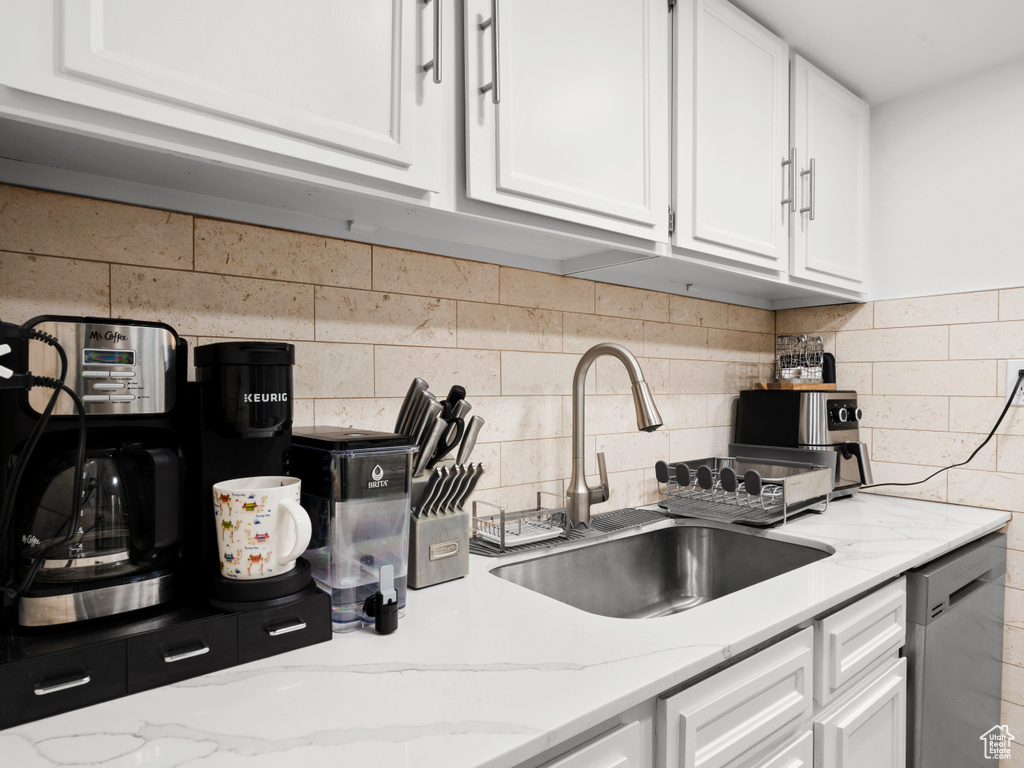 Kitchen with stainless steel dishwasher, white cabinetry, decorative backsplash, and light stone counters