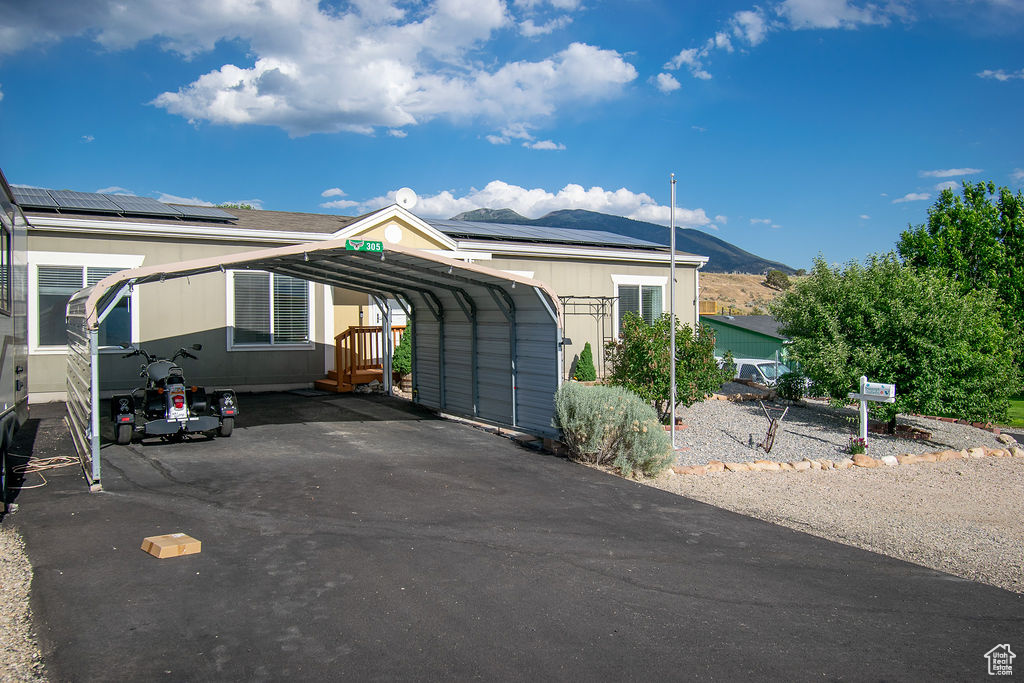 View of front of property featuring driveway, a carport, a mountain view, and roof mounted solar panels