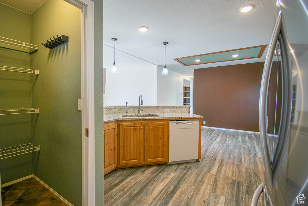 Kitchen with freestanding refrigerator, dishwasher, light stone counters, hanging light fixtures, and wood finished floors