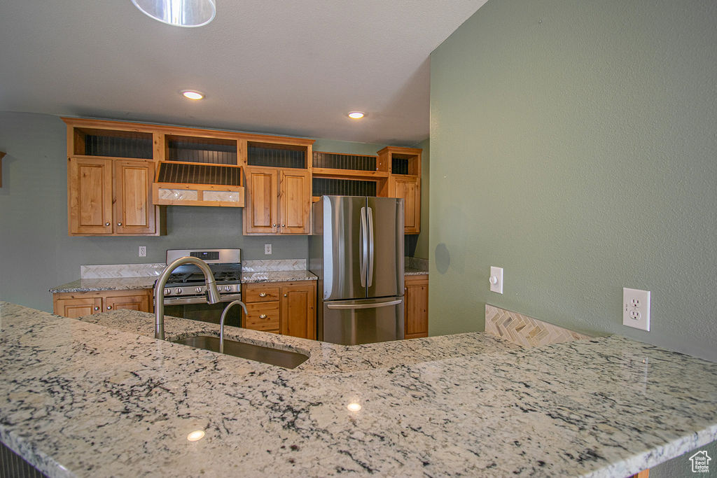 Kitchen featuring stainless steel appliances, open shelves, light stone counters, brown cabinets, and recessed lighting