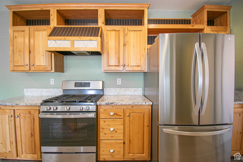 Kitchen featuring stainless steel appliances, custom range hood, open shelves, and light stone countertops