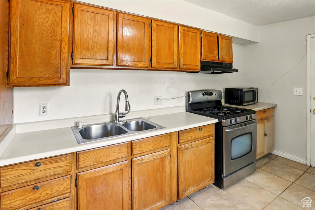 Kitchen with gas range, black microwave, under cabinet range hood, light countertops, and brown cabinets