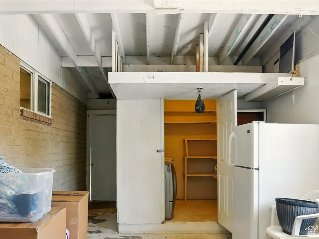 Kitchen with freestanding refrigerator, concrete flooring, brown cabinets, and washer / dryer