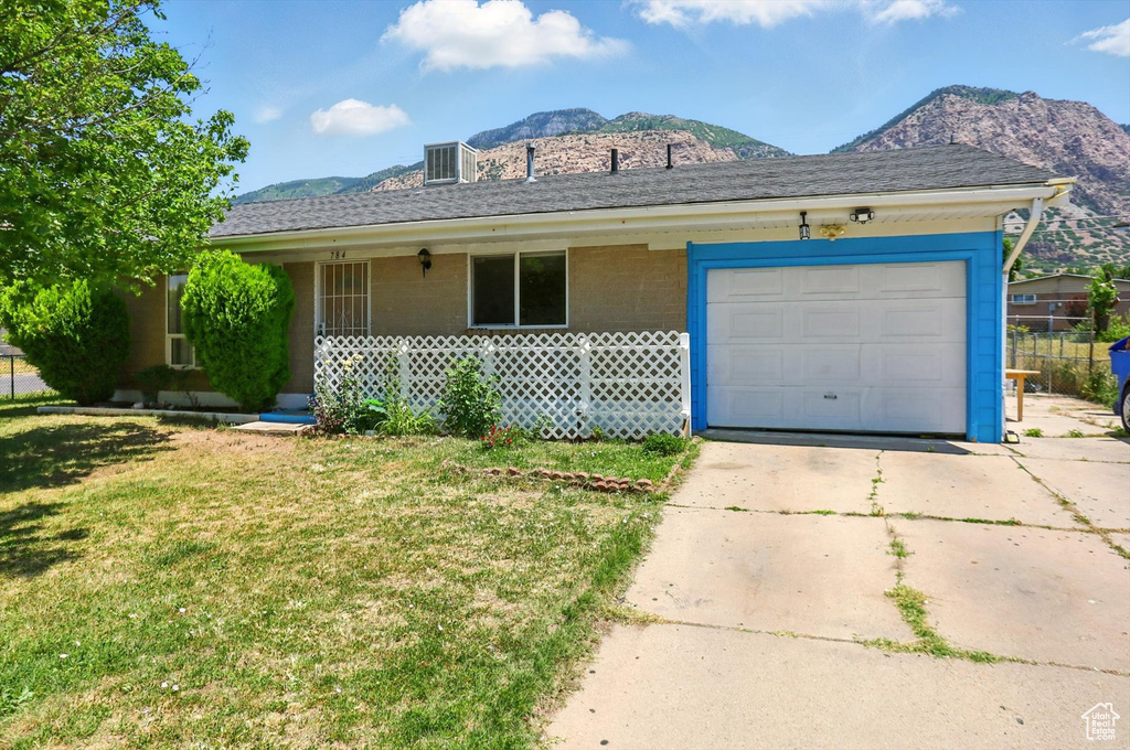Single story home featuring a mountain view, concrete driveway, a front lawn, a porch, and a garage