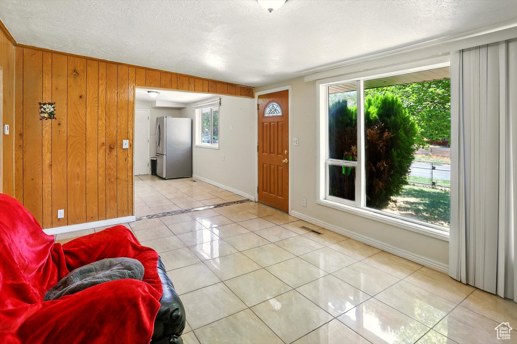 Entrance foyer with light tile patterned flooring, a textured ceiling, and wood walls