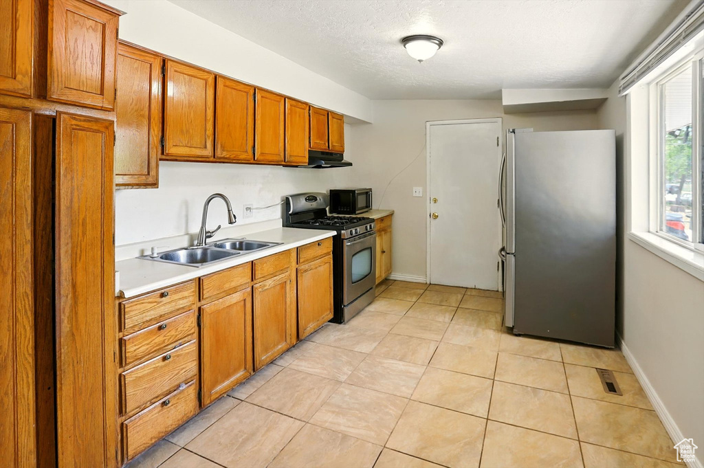 Kitchen with appliances with stainless steel finishes, under cabinet range hood, brown cabinets, and light countertops