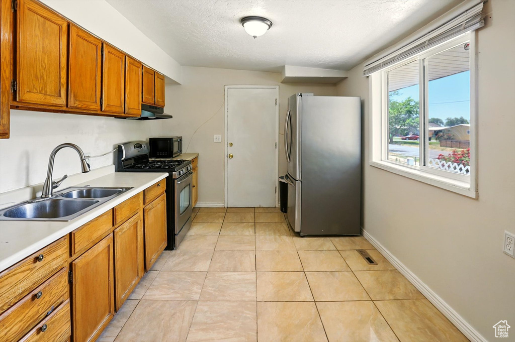 Kitchen with appliances with stainless steel finishes, brown cabinetry, light countertops, under cabinet range hood, and light tile patterned floors