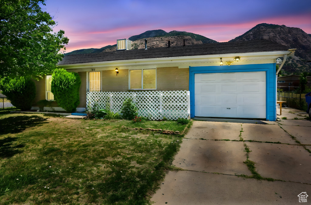 Ranch-style home featuring a mountain view, concrete driveway, a garage, and a front yard