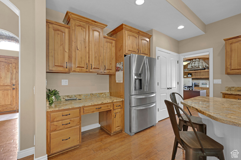 Kitchen with stainless steel refrigerator with ice dispenser, built in study area, light wood-style flooring, a kitchen bar, and light stone countertops
