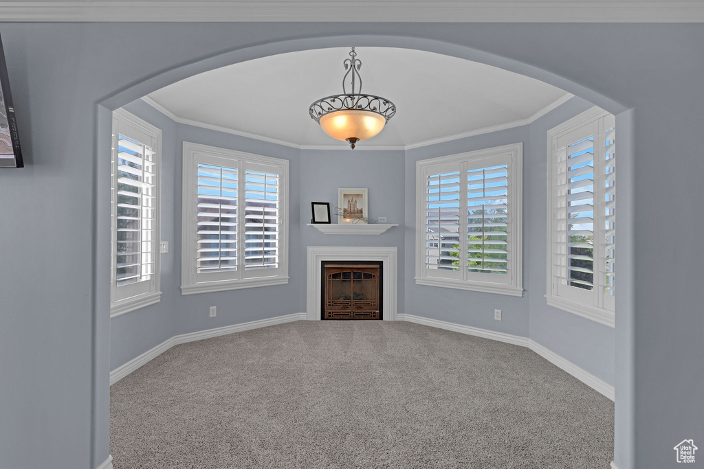 Unfurnished living room with plenty of natural light, a fireplace, arched walkways, and crown molding
