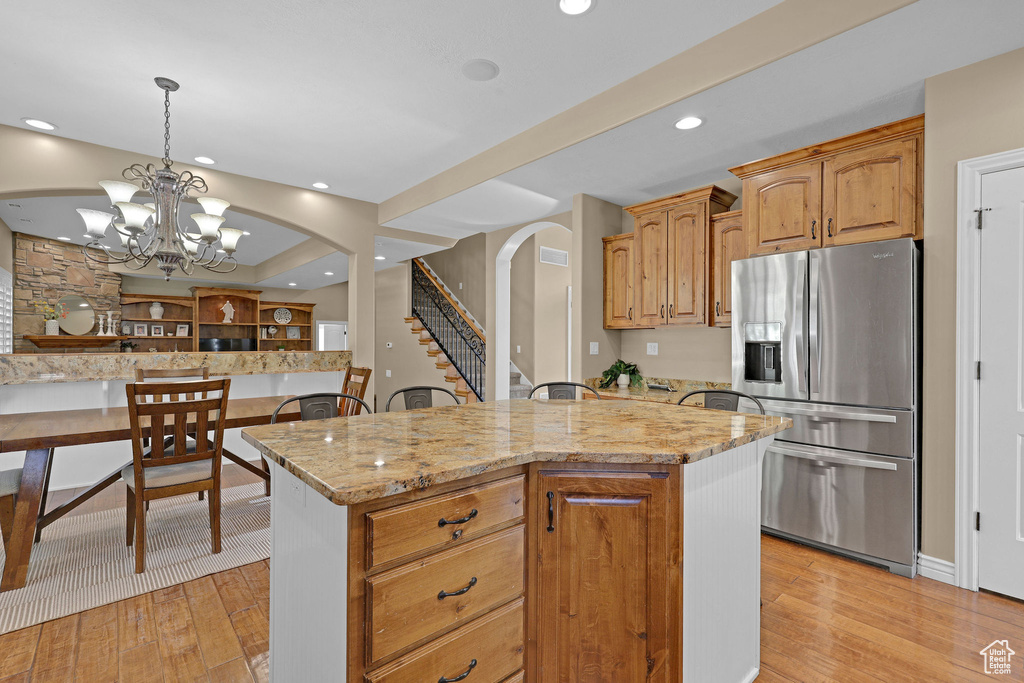 Kitchen featuring stainless steel fridge with ice dispenser, arched walkways, light stone countertops, light wood-type flooring, and a center island