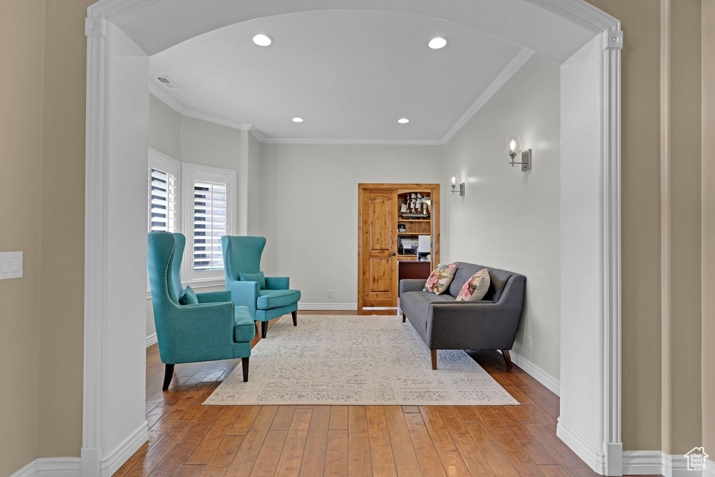 Living area with arched walkways, wood-type flooring, ornamental molding, and recessed lighting