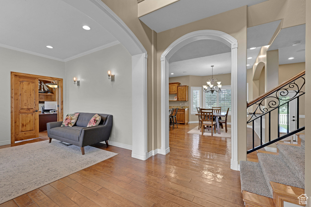 Foyer entrance featuring arched walkways, light wood finished floors, stairway, ornamental molding, and a chandelier