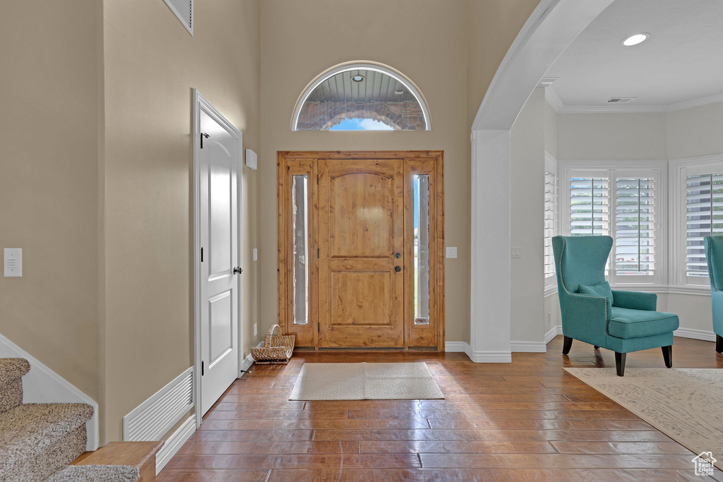 Foyer entrance with arched walkways, wood-type flooring, stairs, recessed lighting, and ornamental molding
