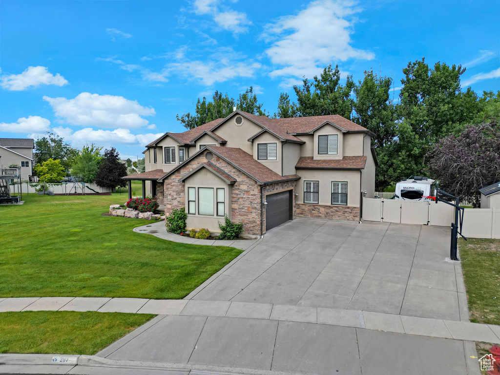 View of front of property with stucco siding, a gate, driveway, stone siding, and a garage