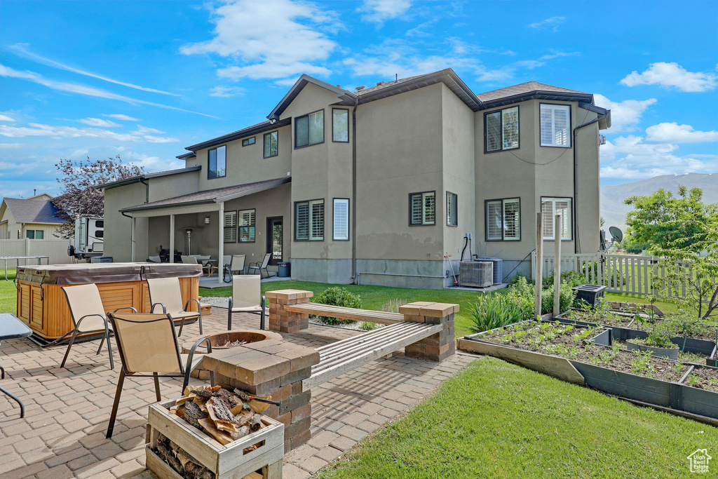 Back of property with a hot tub, an outdoor fire pit, a patio area, and a garden