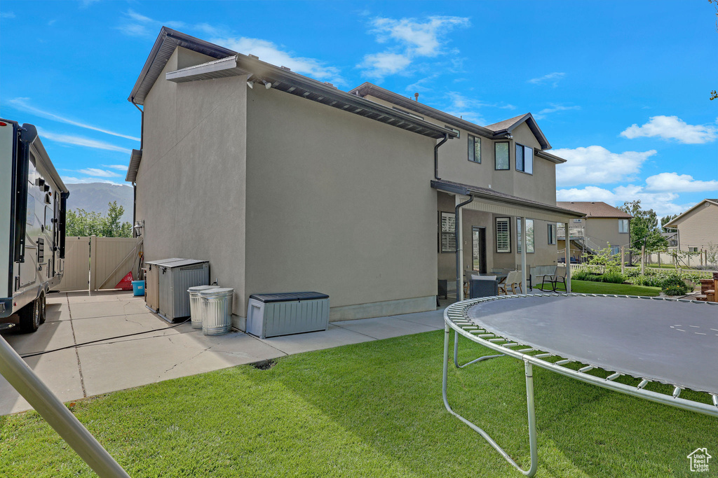 Rear view of house with a trampoline, a patio, a gate, stucco siding, and a residential view