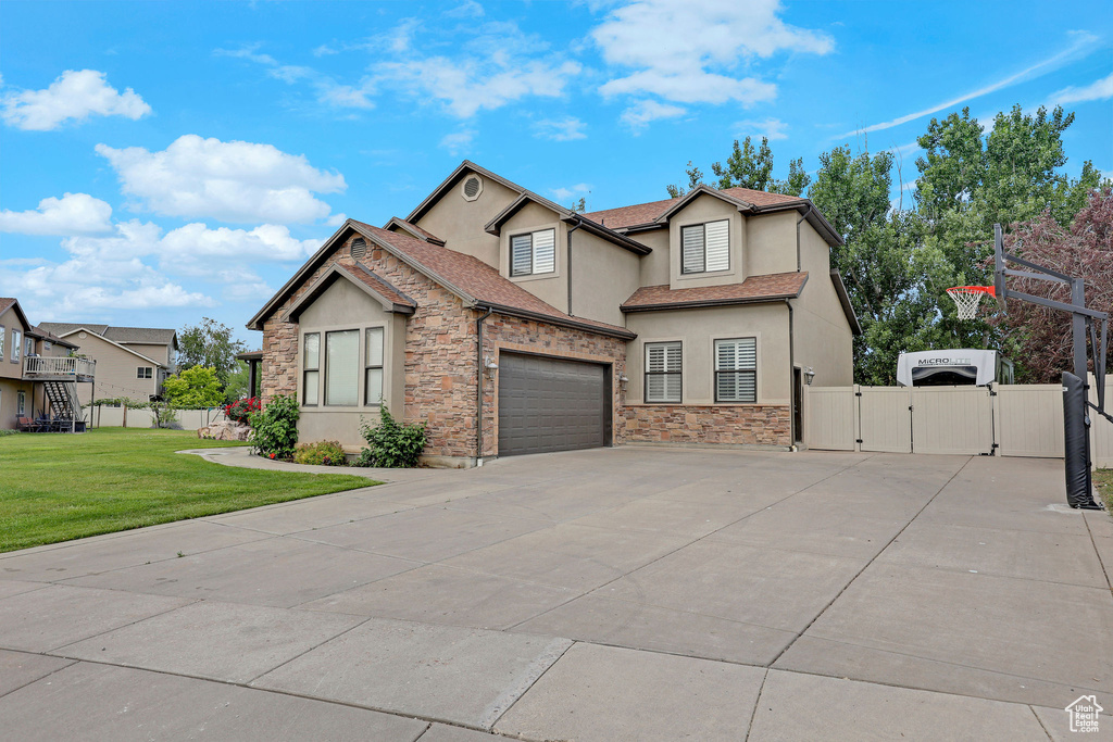 View of front facade with a gate, stucco siding, driveway, and stone siding