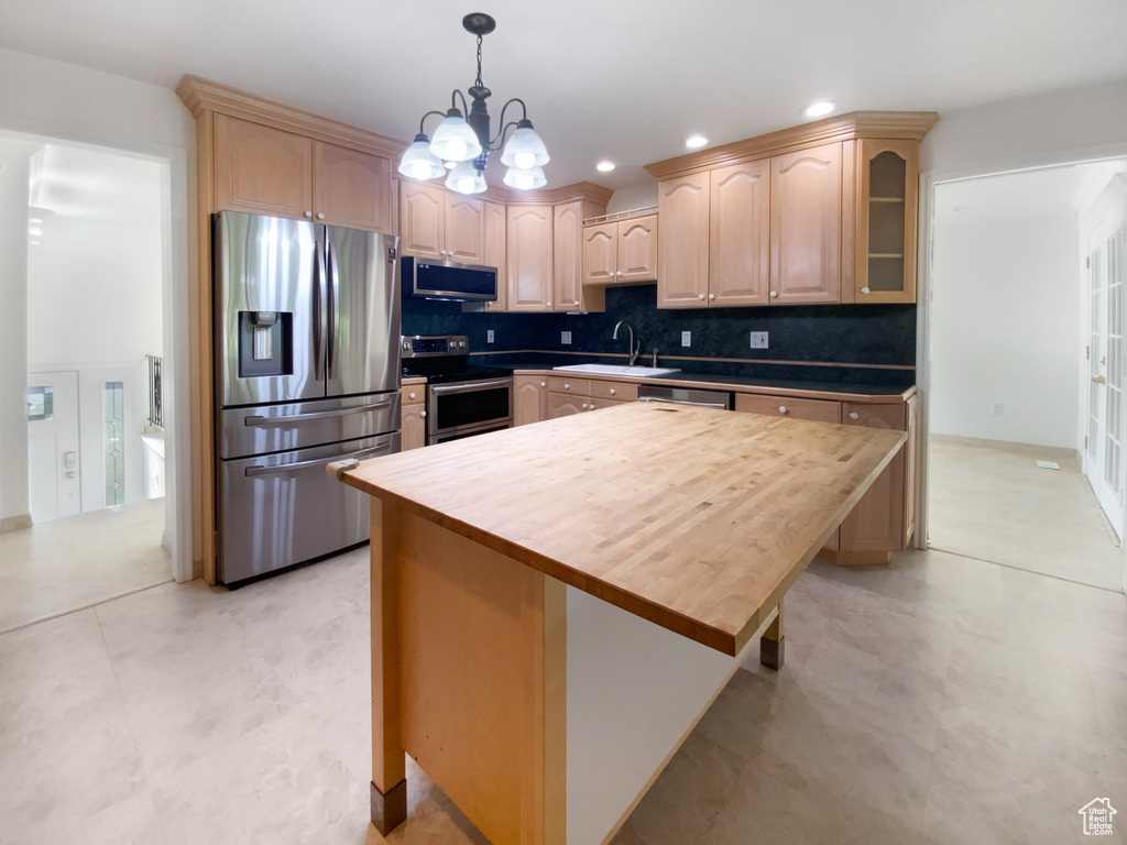 Kitchen with appliances with stainless steel finishes, light brown cabinets, glass insert cabinets, tasteful backsplash, and a chandelier