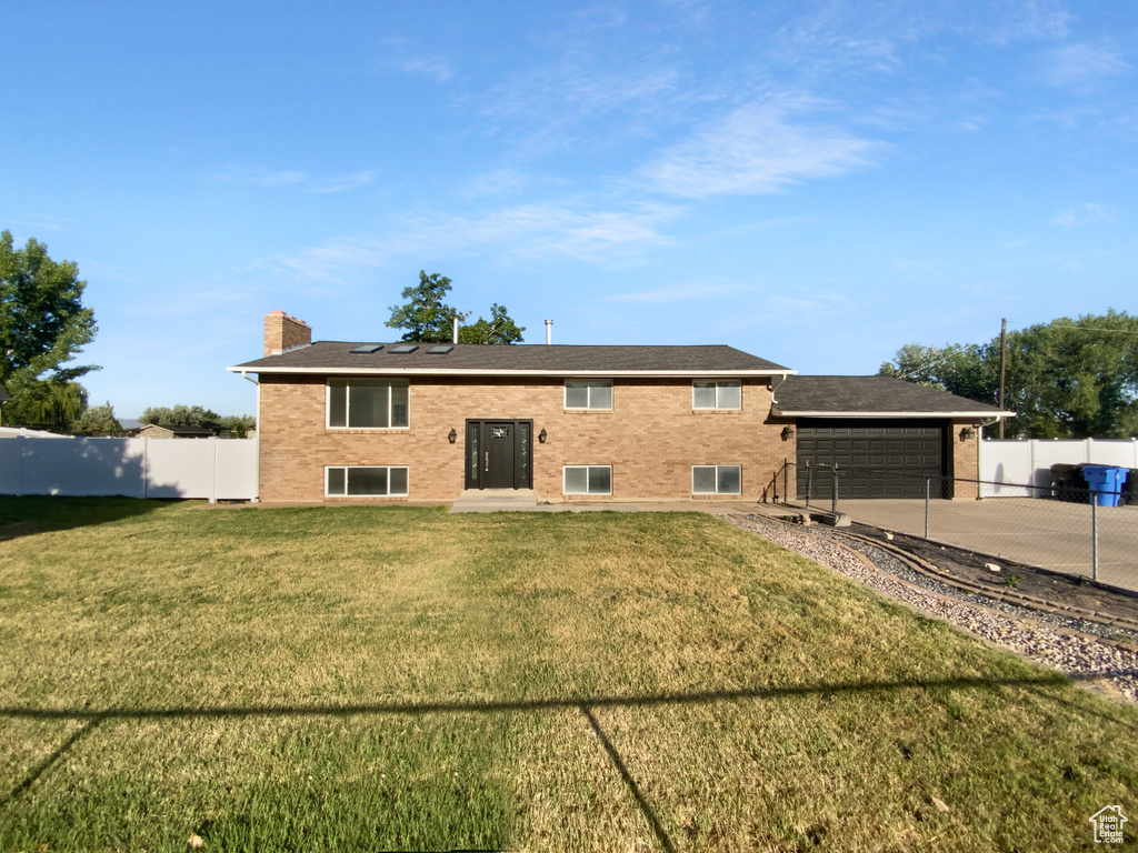 Rear view of property with driveway, a chimney, brick siding, and an attached garage