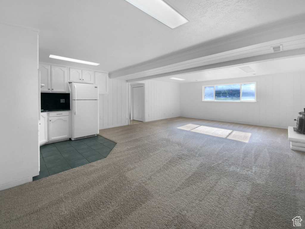 Unfurnished living room with carpet, a wood stove, tile patterned floors, and beam ceiling