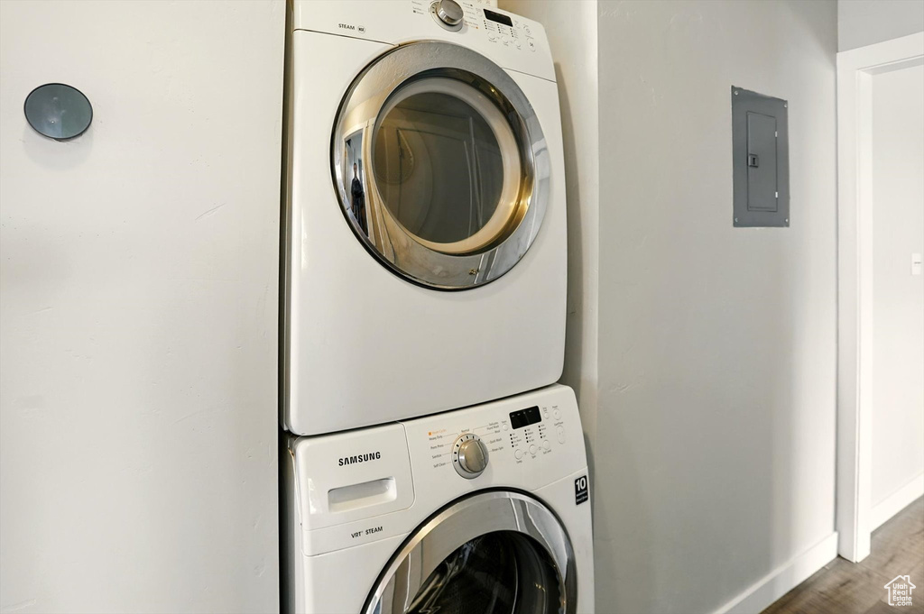 Laundry area with stacked washer / dryer, electric panel, and wood finished floors